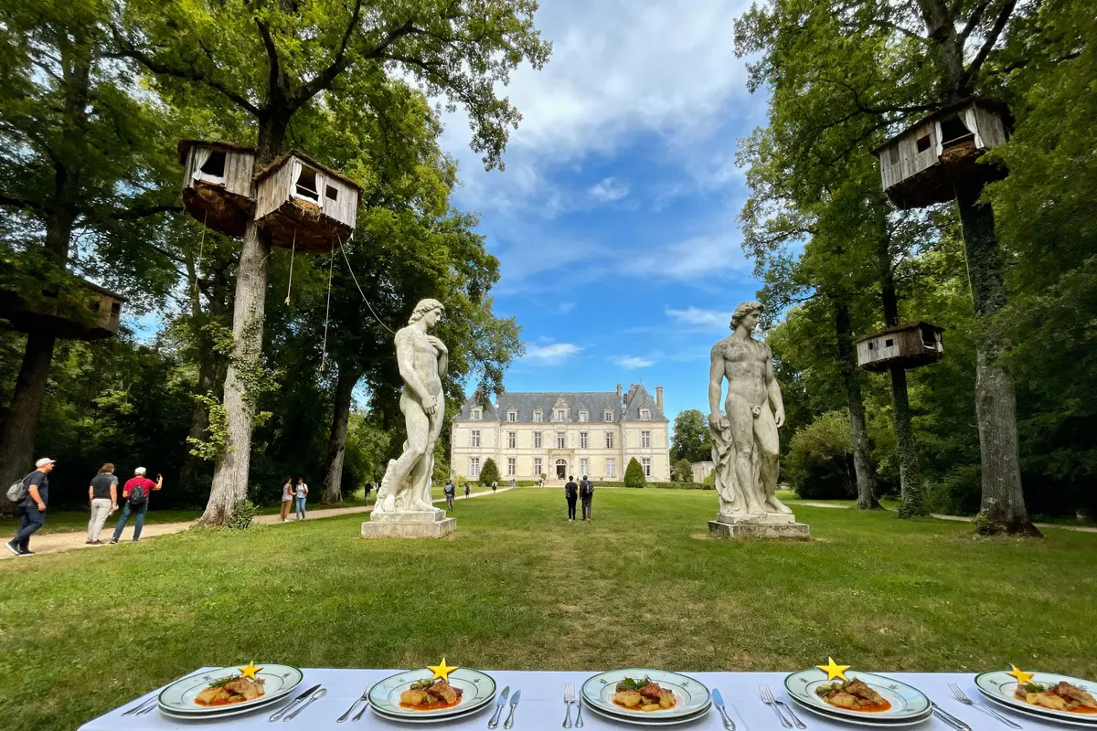pexels-michal-pech-213601-757318 (1) Château entouré de statues, cabanes dans les arbres, et table dressée avec repas raffinés au premier plan.