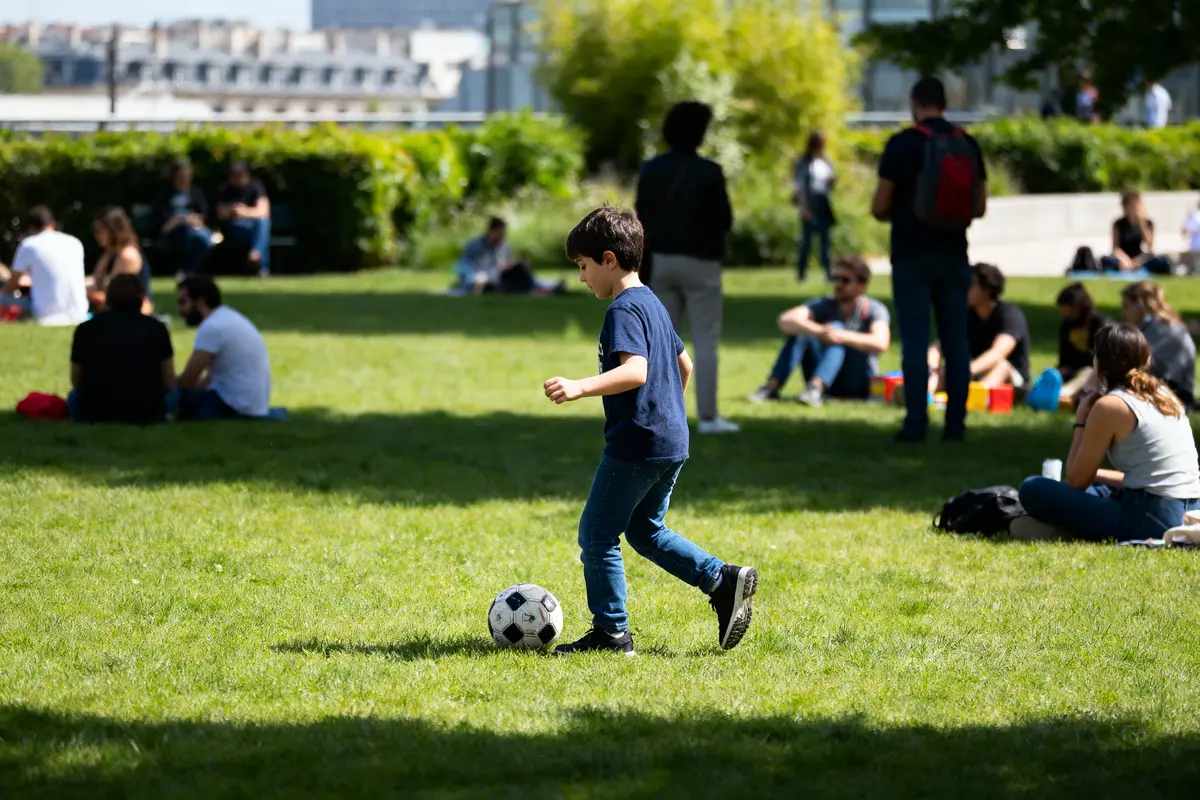 pexels-michal-pech-213601-757318 (1) Garçon jouant au football dans un parc verdoyant, entouré de personnes assises sur l'herbe.