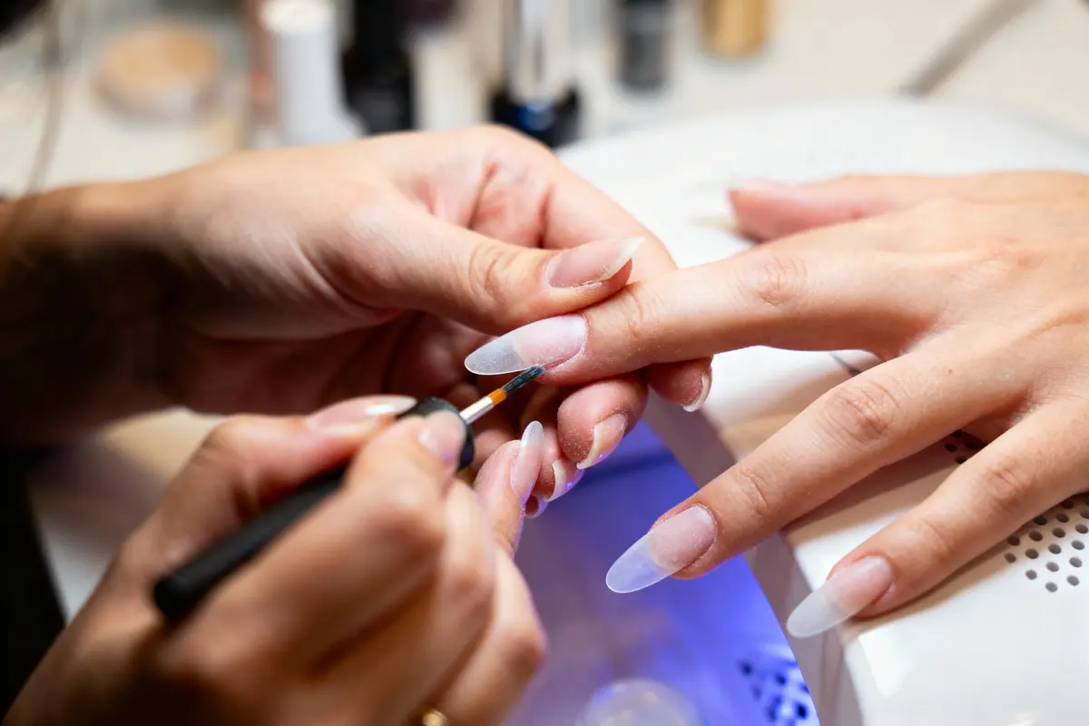 pexels-michal-pech-213601-757318 (1) Manucure en cours avec application de vernis ou gel sur ongles longs et pointus, lumière LED en arrière-plan.
