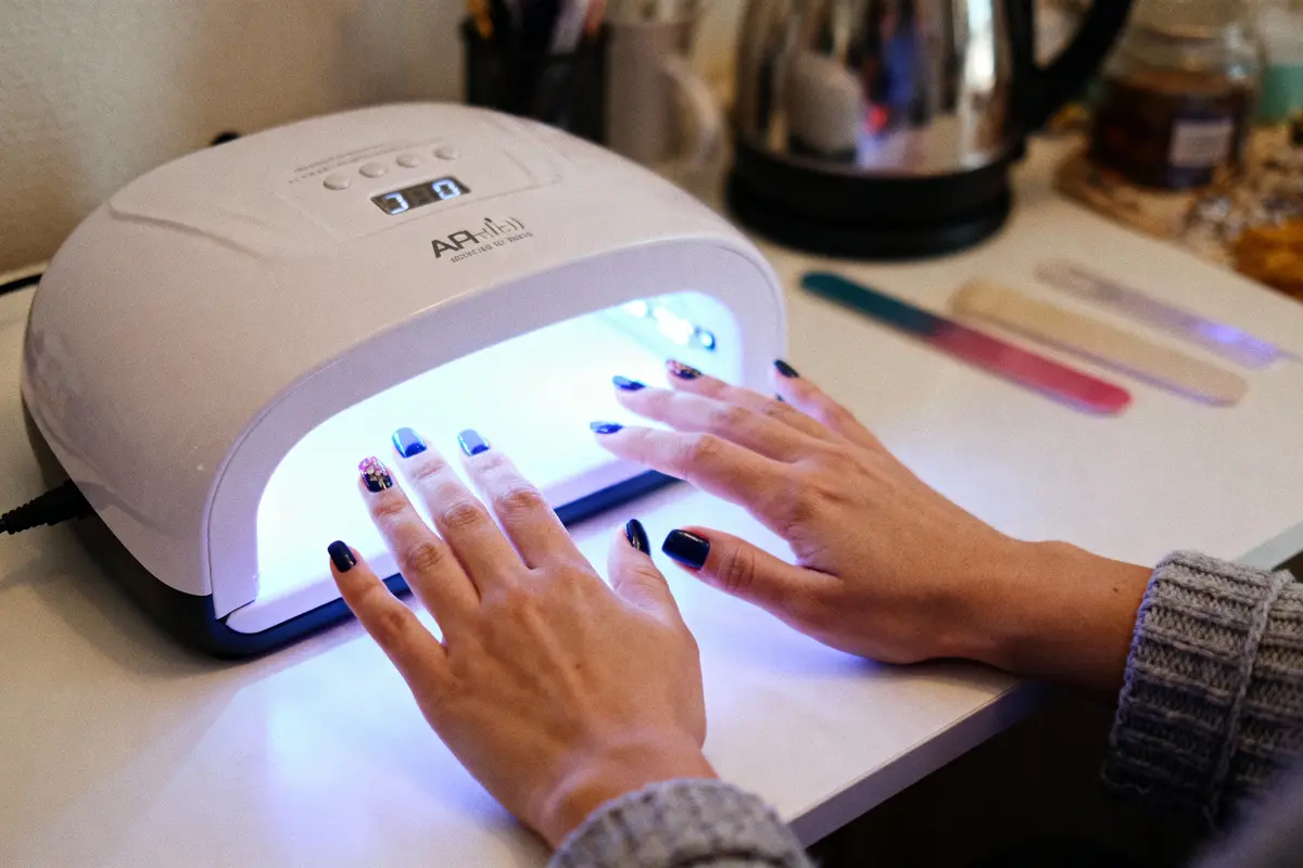 Deux mains avec vernis sous une lampe UV pour manucure sur une table avec limes à ongles.