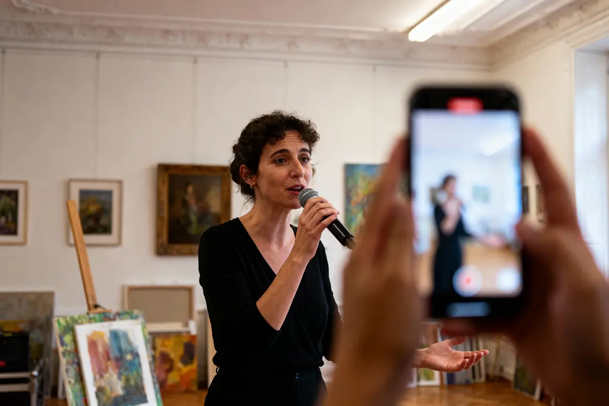 Une femme chante dans une galerie d'art, filmée par un smartphone au premier plan.