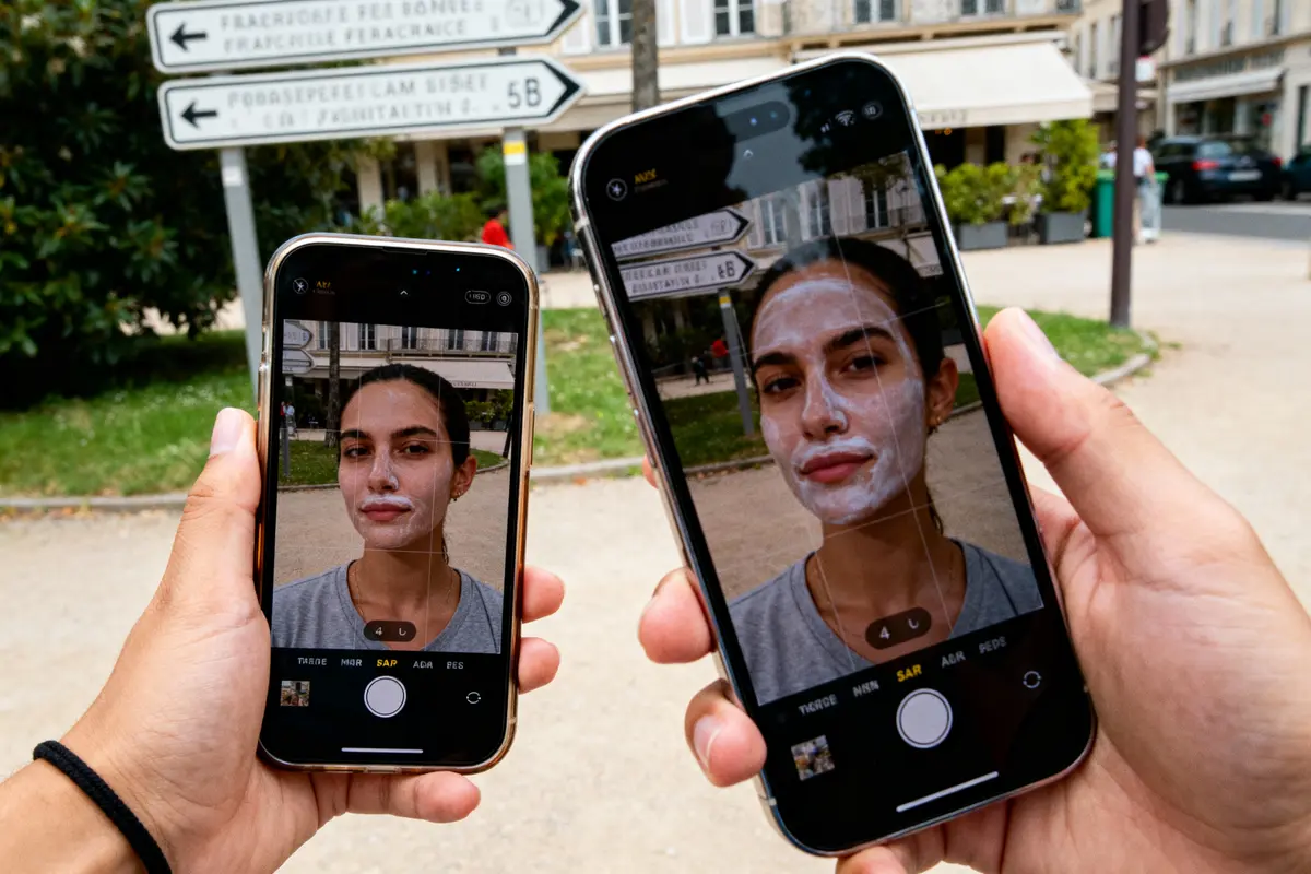 Deux smartphones photographient une personne avec un masque facial, pancartes en arrière-plan dans la rue.