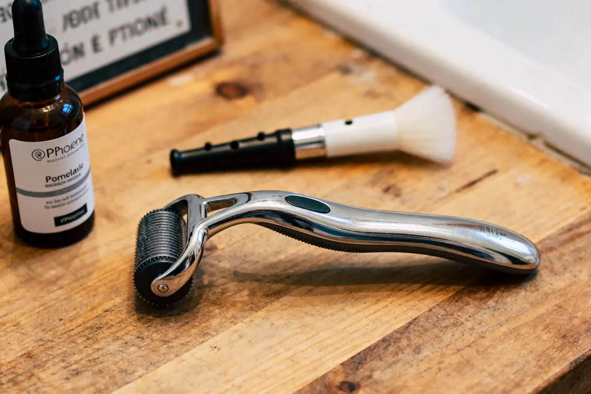 Roller en métal, flacon d'huile, pinceau de rasage sur table en bois dans une salle de bain.