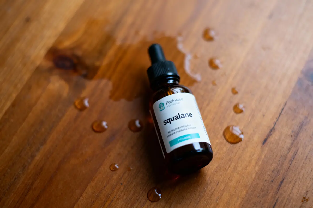 pexels-michal-pech-213601-757318 (1) Flacon de squalane sur table en bois mouillée. Produit cosmétique avec compte-gouttes et gouttes autour.