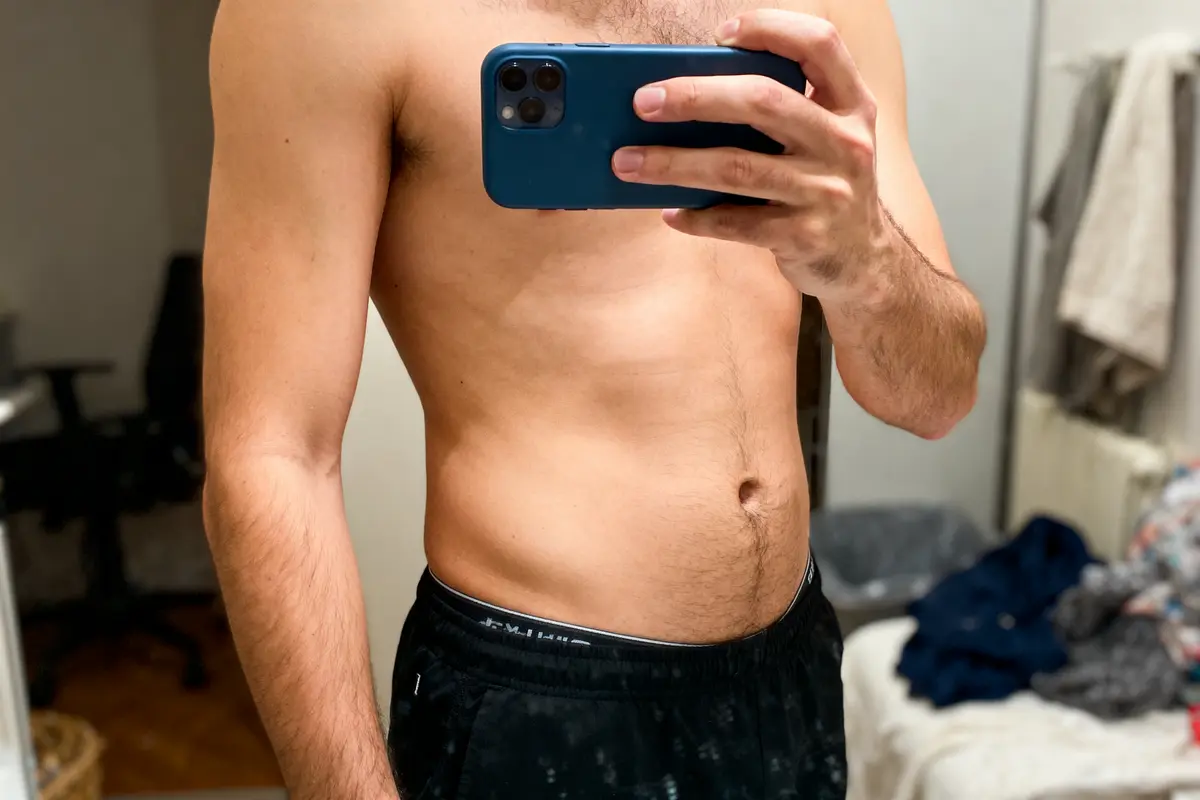 Homme torse nu prenant un selfie dans un miroir, portant un short noir.