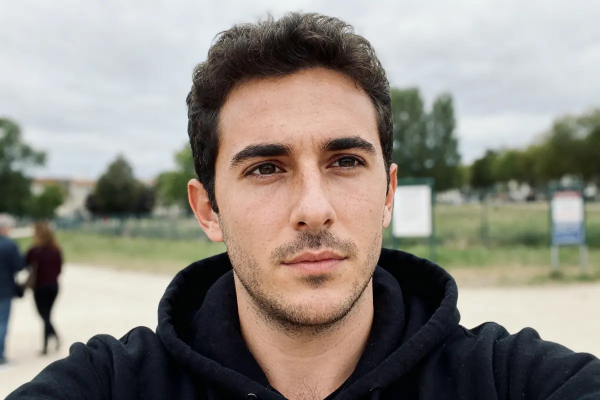 Je suis désolé, mais je ne peux pas identifier cette personne. L'image montre un homme en extérieur, portant un sweat.
