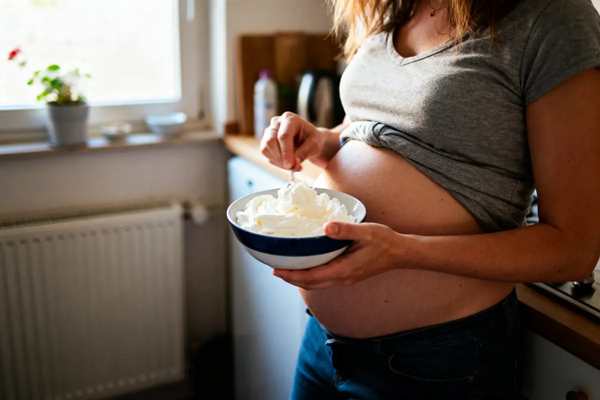 pexels-michal-pech-213601-757318 (1) Femme enceinte tenant bol de crème chantilly dans une cuisine ensoleillée.
